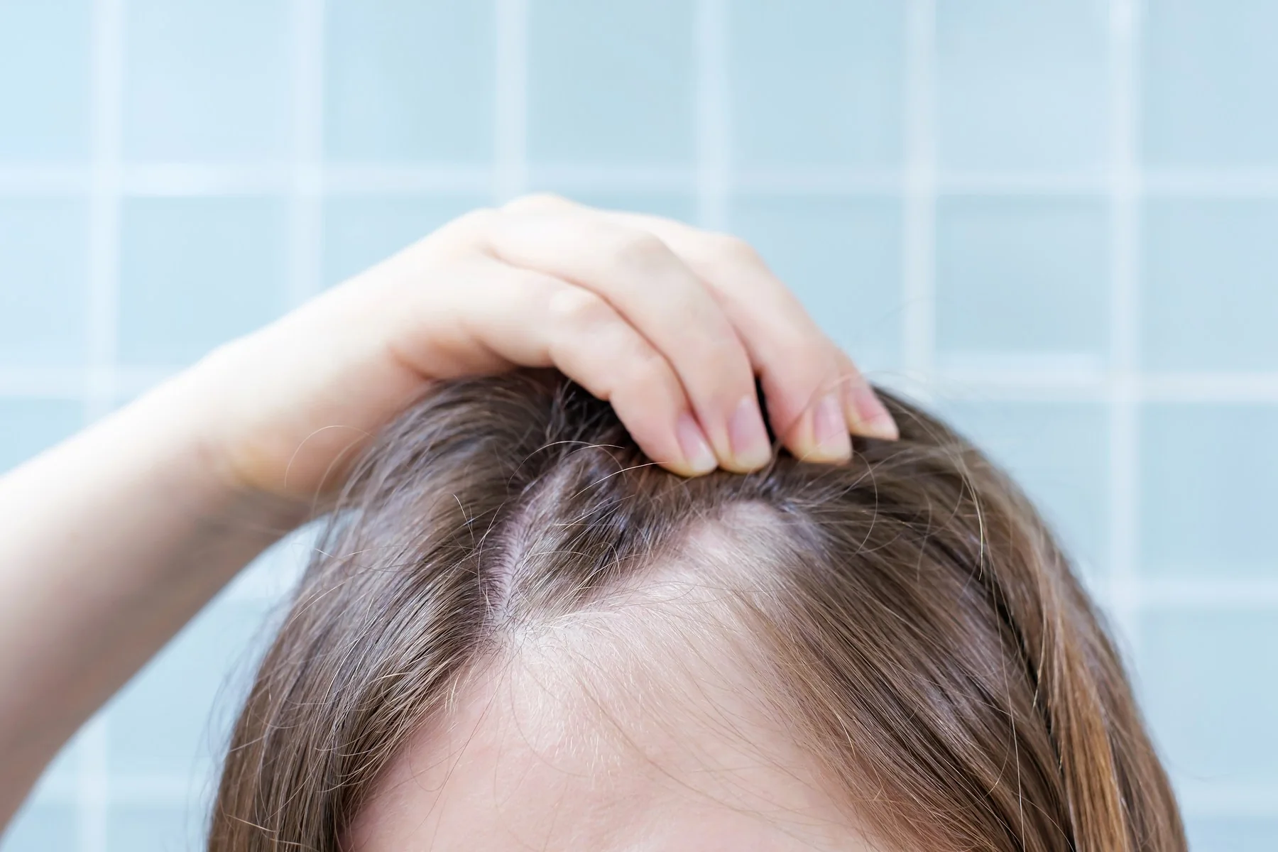 Alopecia areata en Bilbao: mujer que se toca el cabello, en primer plano sobre fondo neutro