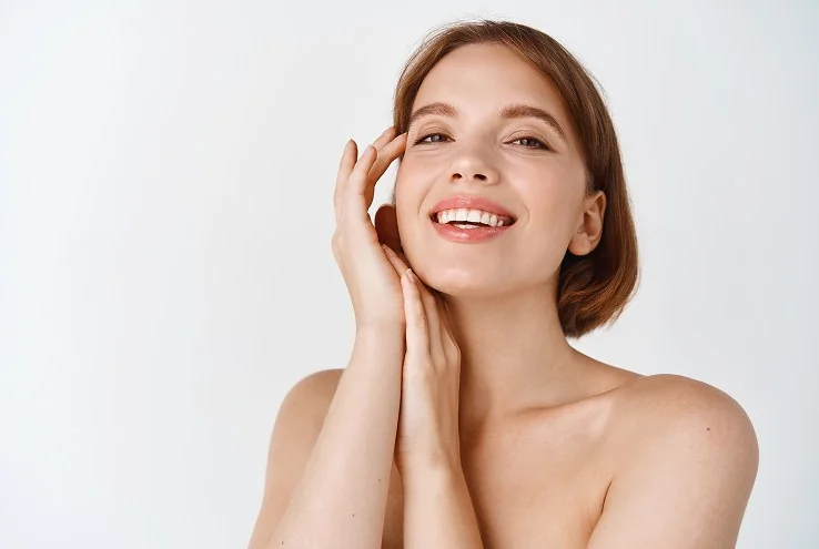 Rejuvenecimiento facial en Bilbao: mujer sonriente tocándose la mejilla